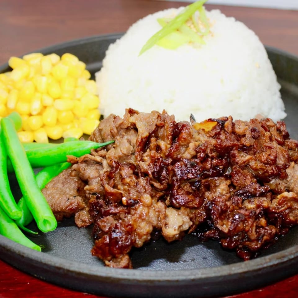 Sizzling beef with rice, corn, and green beans on a black plate.
