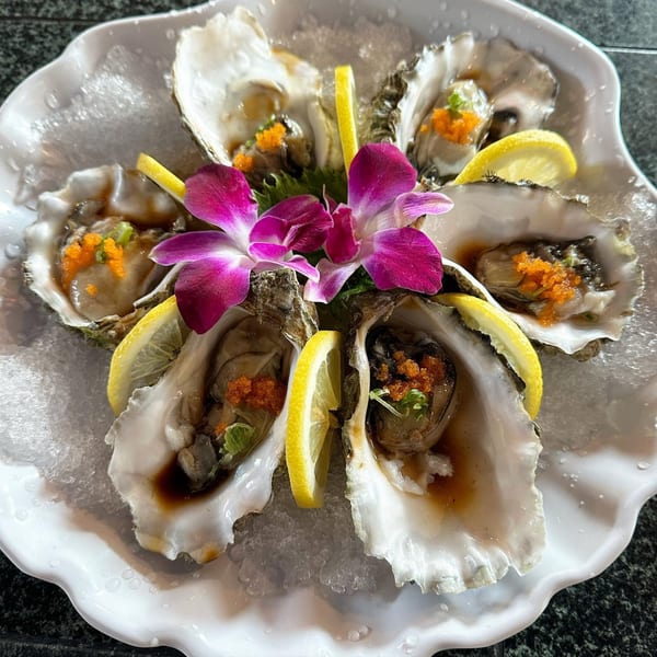 Six oysters on the half shell with lemon, roe, and orchids on a bed of ice.