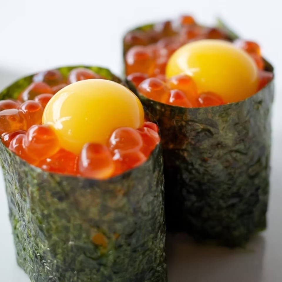 Two gunkan maki sushi pieces with bright orange salmon roe and a raw quail egg yolk.