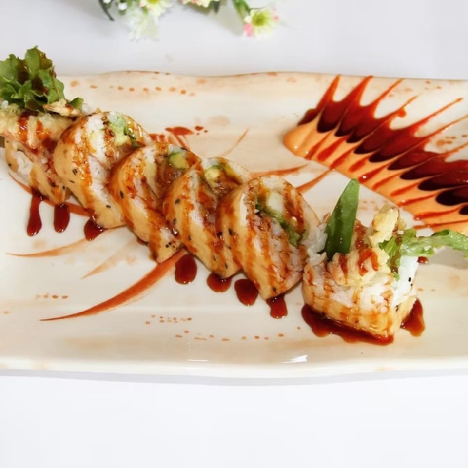 Sushi rolls with sauce drizzle and green garnish on a rectangular plate with decorative sauce.