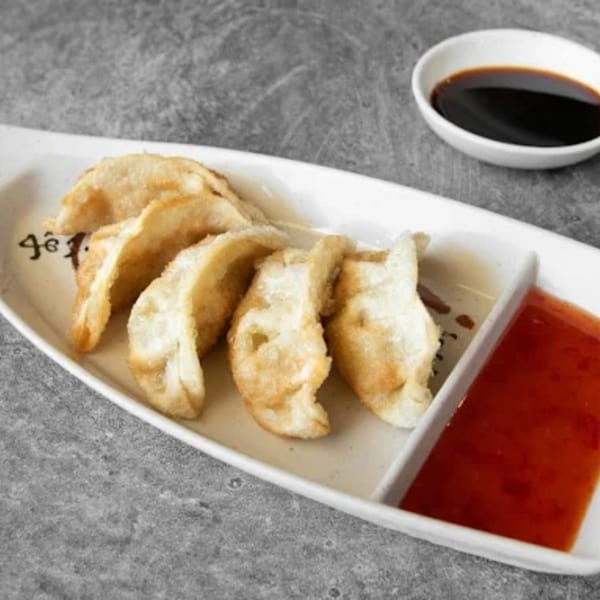 Crispy fried dumplings with sweet chili sauce and soy sauce on a white rectangular plate.