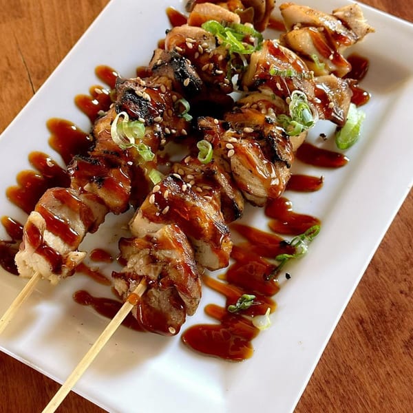 Two skewers of grilled chicken with teriyaki sauce, sesame seeds, and green onions on a white plate.
