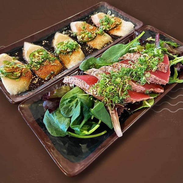 Two rectangular plates of Japanese food, one with seared tuna and greens, the other with white fish.