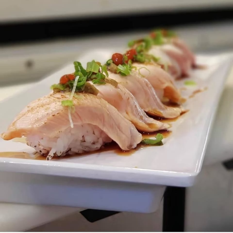 A row of salmon nigiri sushi with green onions and red roe on a white rectangular plate.