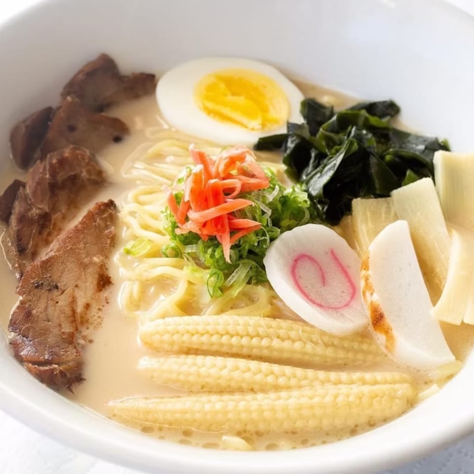 Close-up of a ramen bowl with pork, egg, seaweed, baby corn, and fish cake.