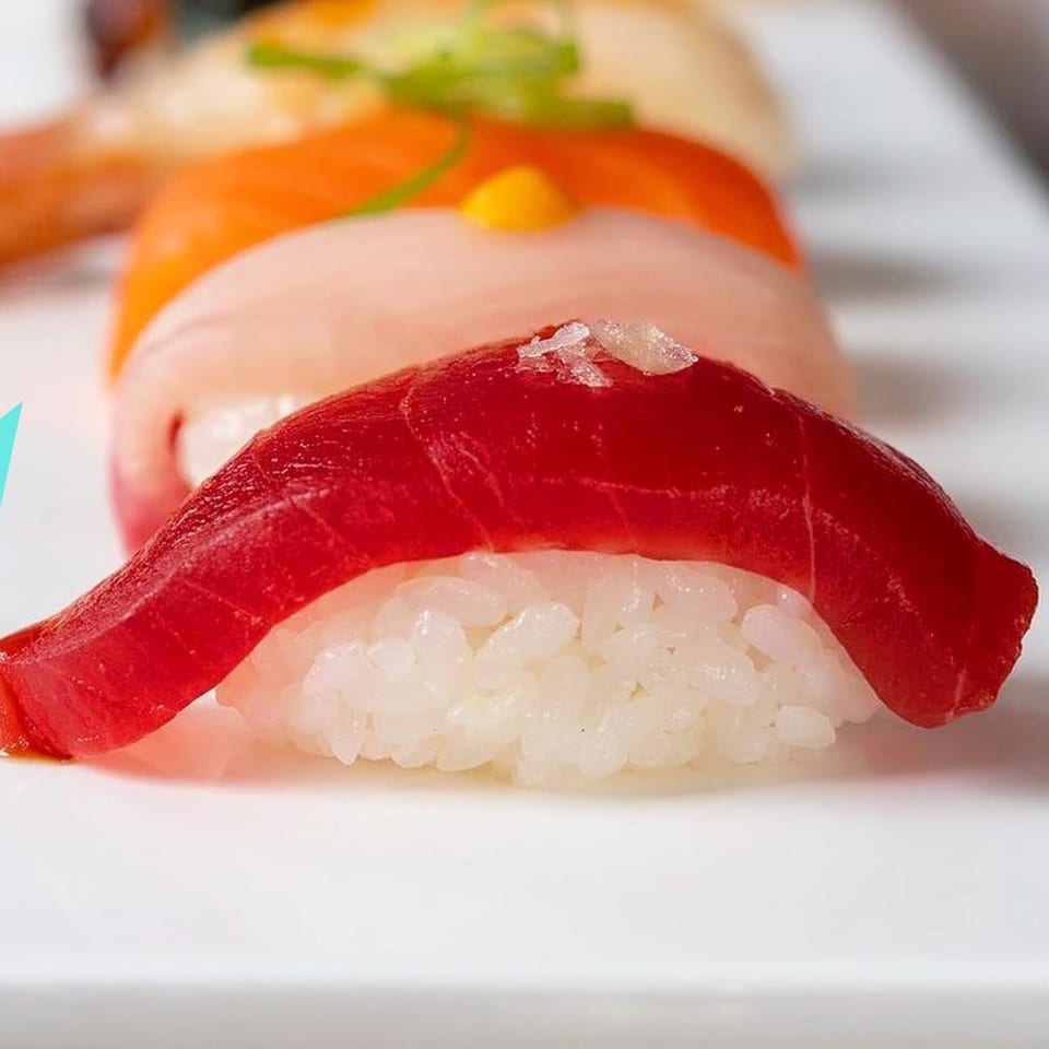 Close-up of a vibrant red tuna nigiri with sea salt flakes, in a row of various sushi.