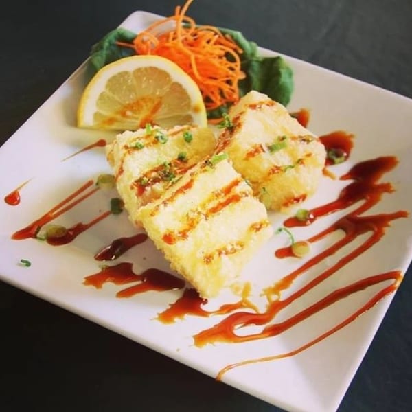 Crispy fried tofu drizzled with sauce, garnished with lemon, shredded carrots, and greens.