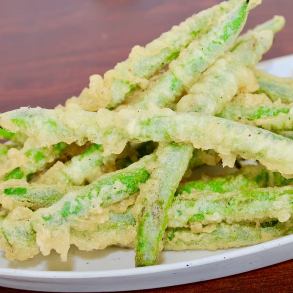 A close-up of a plate piled high with crispy, golden-brown tempura green beans.