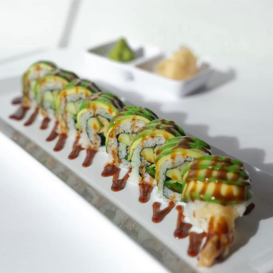 A sushi roll with avocado slices and eel sauce, served with wasabi and ginger.